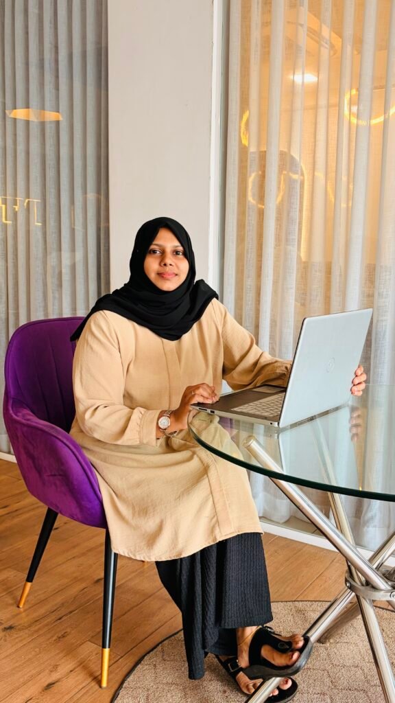 Freelance digital marketer in Malappuram, Kerala, Murshidha .k is working on a laptop in a professional setting. She is seated at a table, using her laptop while focusing on digital marketing work. This image represents her work as a freelance digital marketer in Malappuram, Kerala, providing digital marketing services and helping businesses build their online presence.